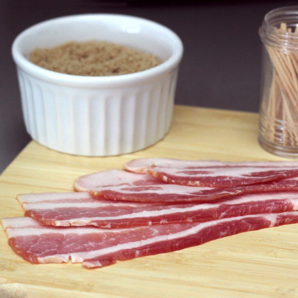Bacon strips on a wooden carving board with brown sugar and toothpicks.
